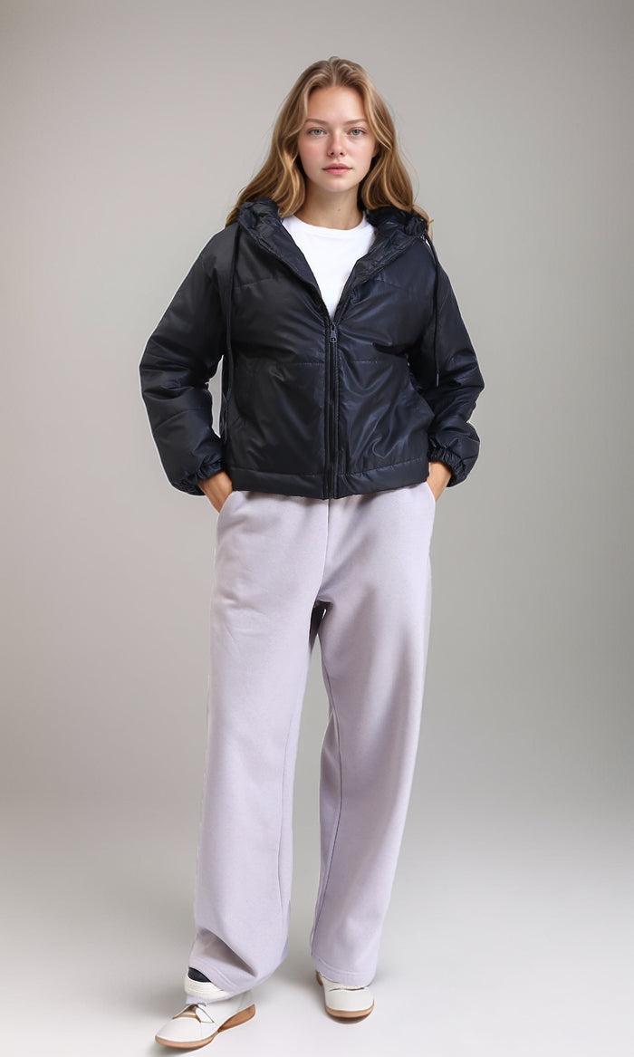Person wearing a black puffer jacket and light gray pants on a plain background