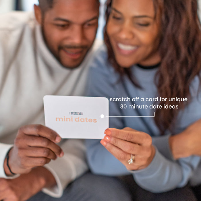 Laughing couple reacting to a revealed Mini Date challenge, enjoying spontaneous quality time together.