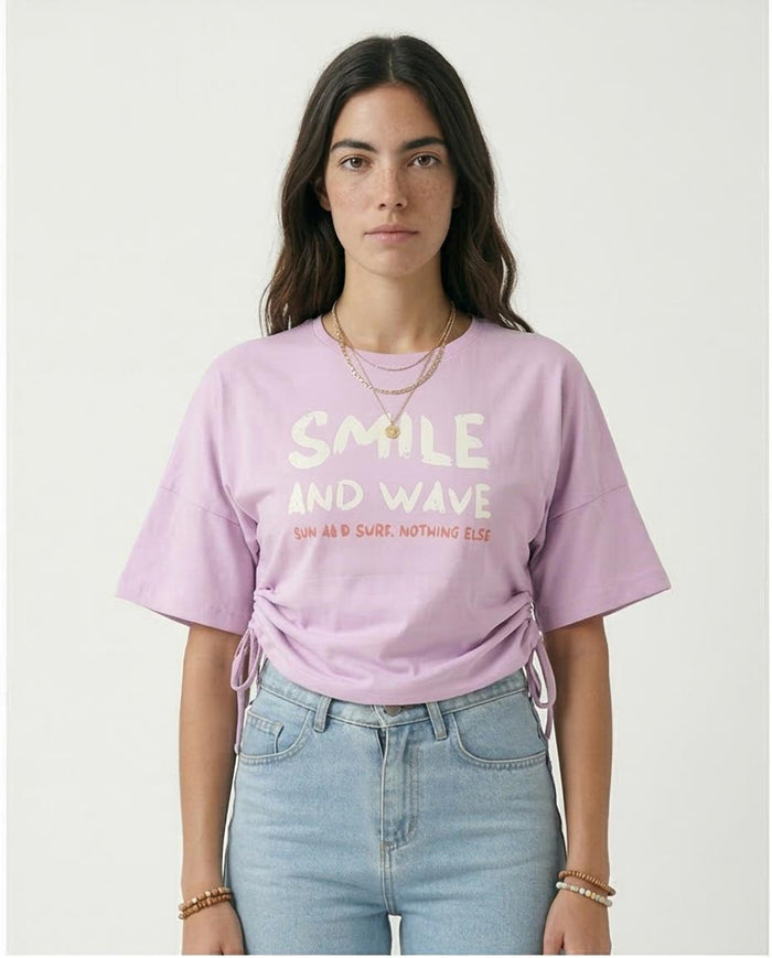 Person wearing a light purple t-shirt with text, standing against a plain background