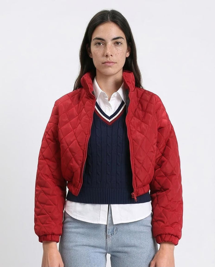 Person wearing a red quilted jacket over a navy sweater with a white shirt on a plain background