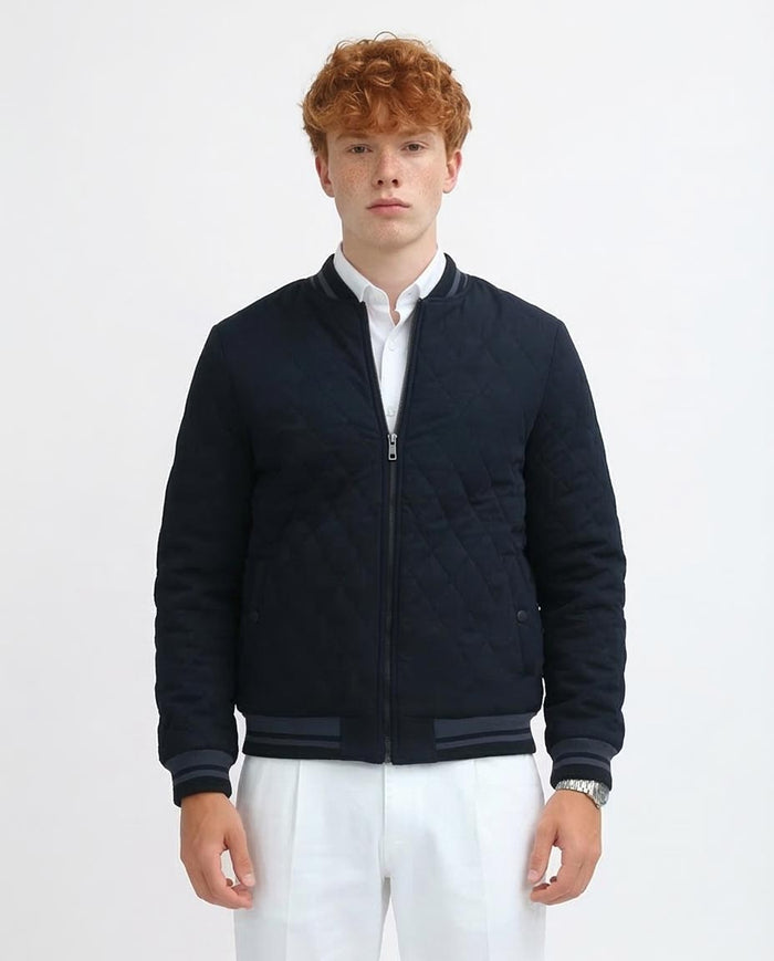 Man wearing a navy quilted jacket over a white shirt on a light gray background