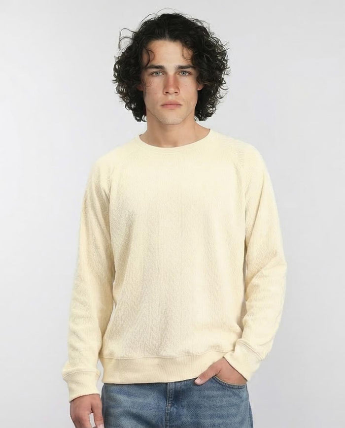 Man wearing a light yellow sweater and blue jeans against a plain background