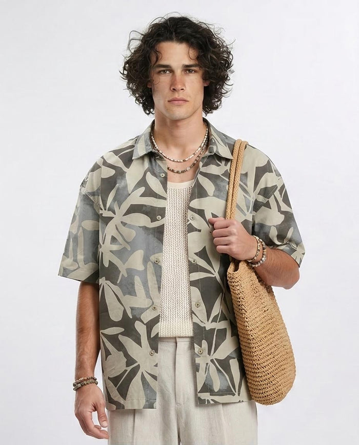 Man wearing a patterned shirt holding a woven bag on a white background