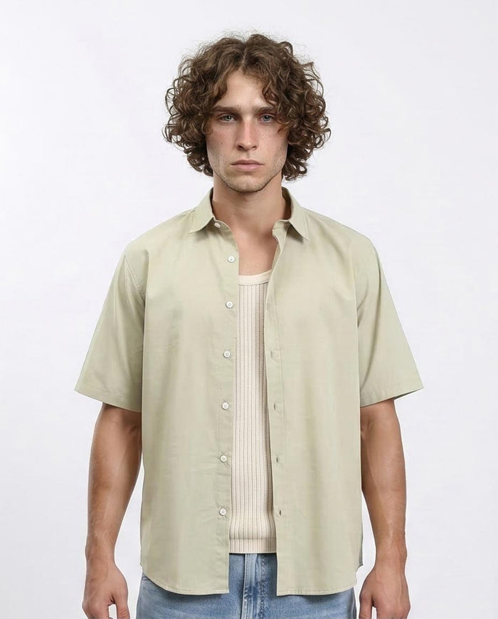 Man wearing a light green button-up shirt over a striped shirt on a white background