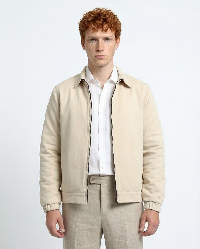 Man wearing a beige jacket over a white shirt and beige pants on a light gray background