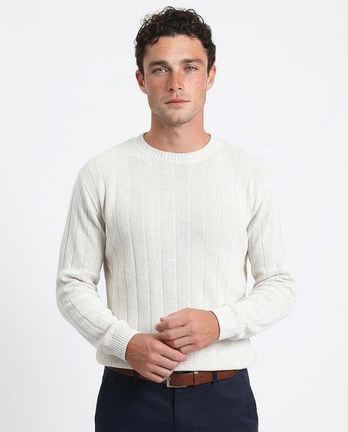 Man wearing a white ribbed sweater and dark pants on a light gray background