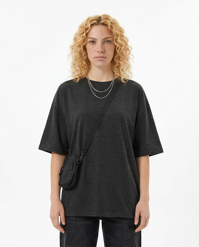Person wearing a black oversized t-shirt with a crossbody bag on a white background