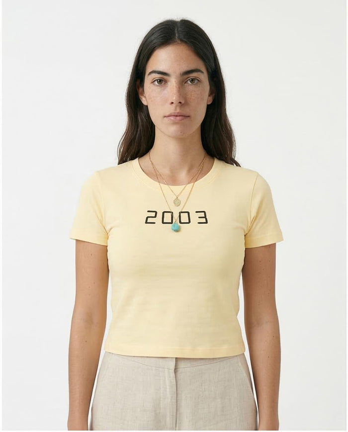 Woman wearing a light yellow t-shirt with '2003' printed on it against a white background