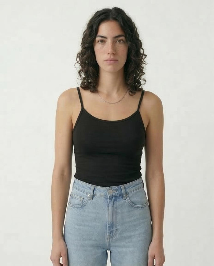 Woman wearing a black tank top and light blue jeans against a white background