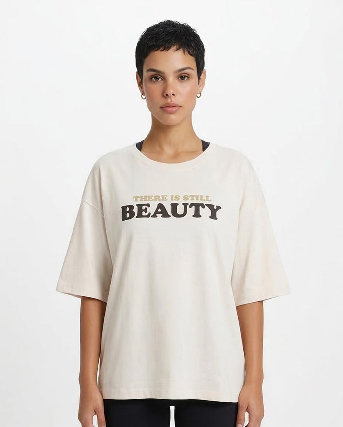 Person wearing a white t-shirt with 'THERE IS STILL BEAUTY' text on a plain background