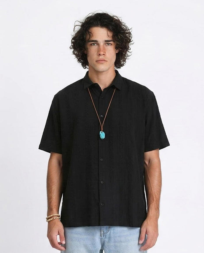 Man wearing a black short-sleeve shirt with a necklace on a white background