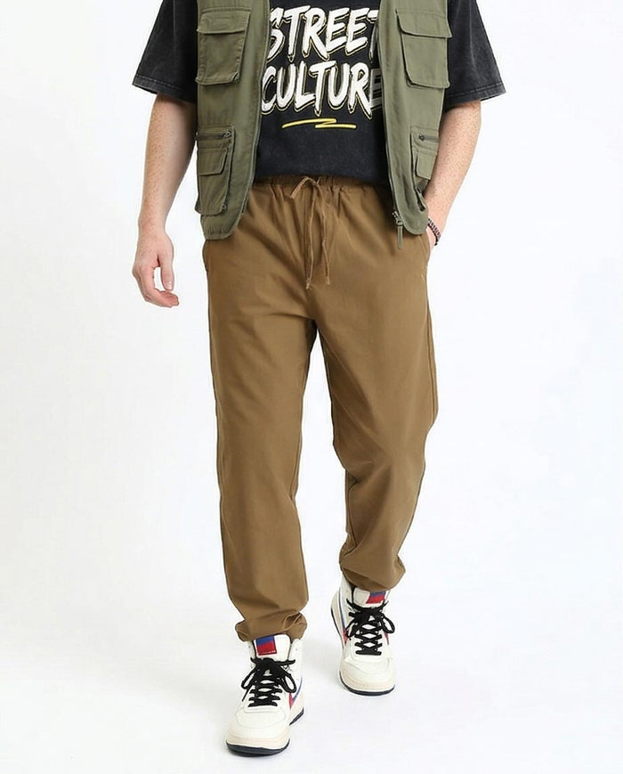 Person wearing a black t-shirt with 'Street Culture' text, green vest, brown pants, and white sneakers on a white background