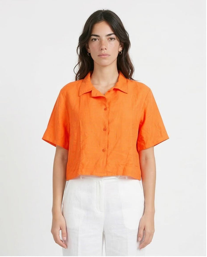 Woman wearing an orange shirt and white pants on a plain background