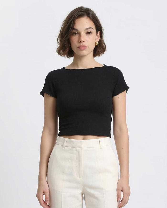 Person wearing a black crop top and white pants on a plain background