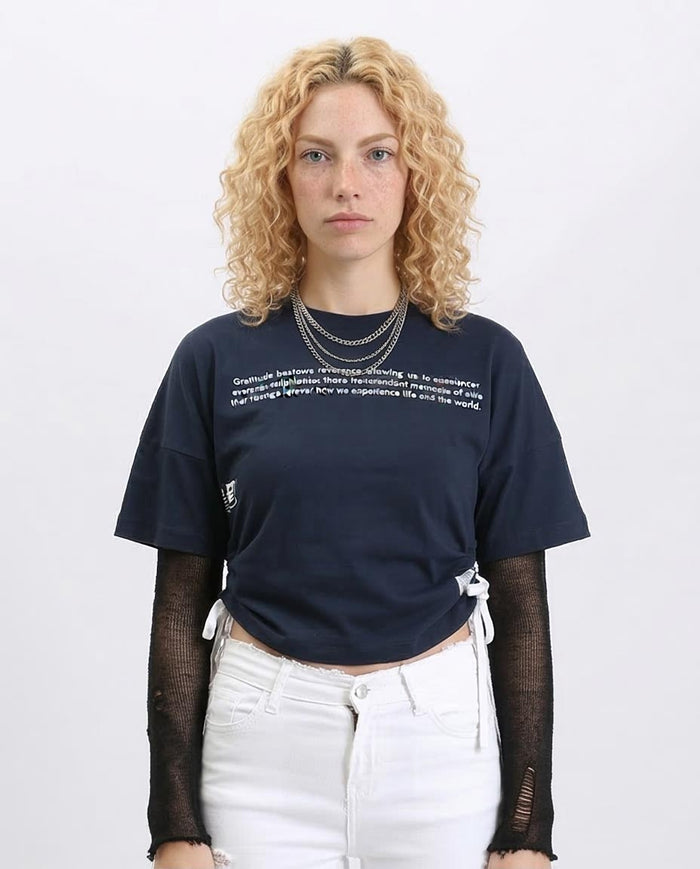 Woman wearing a navy blue t-shirt with text, white pants, and black sheer sleeves on a light gray background